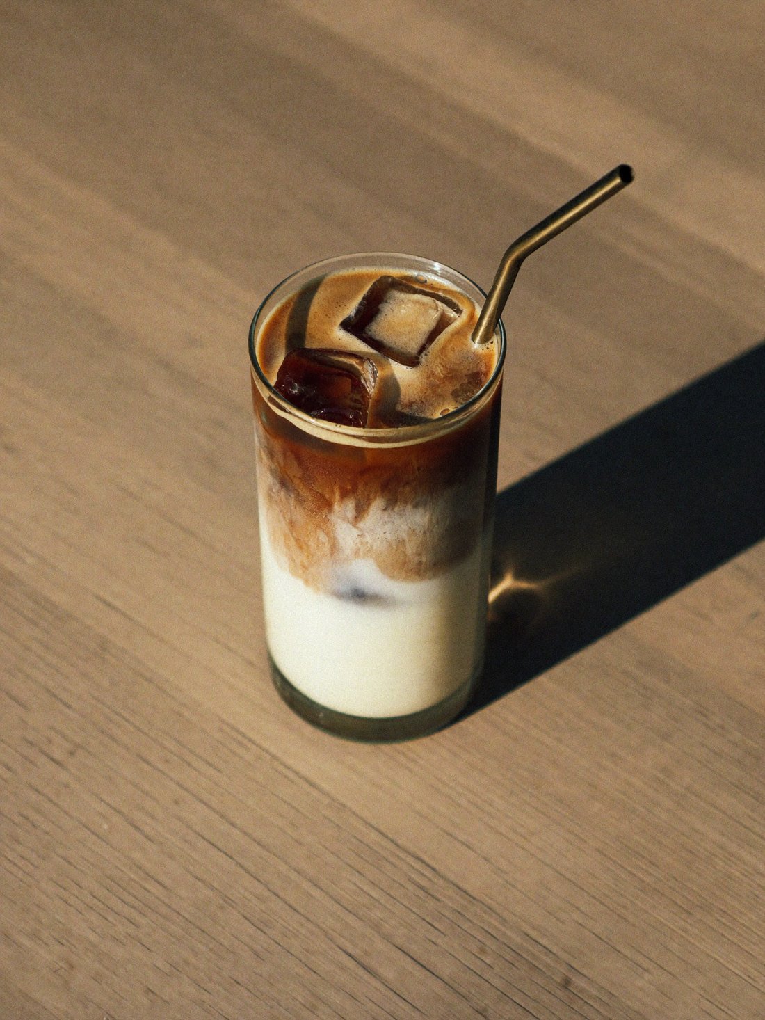 Iced latte em copo de vidro alto com gelo, sob luz de sol