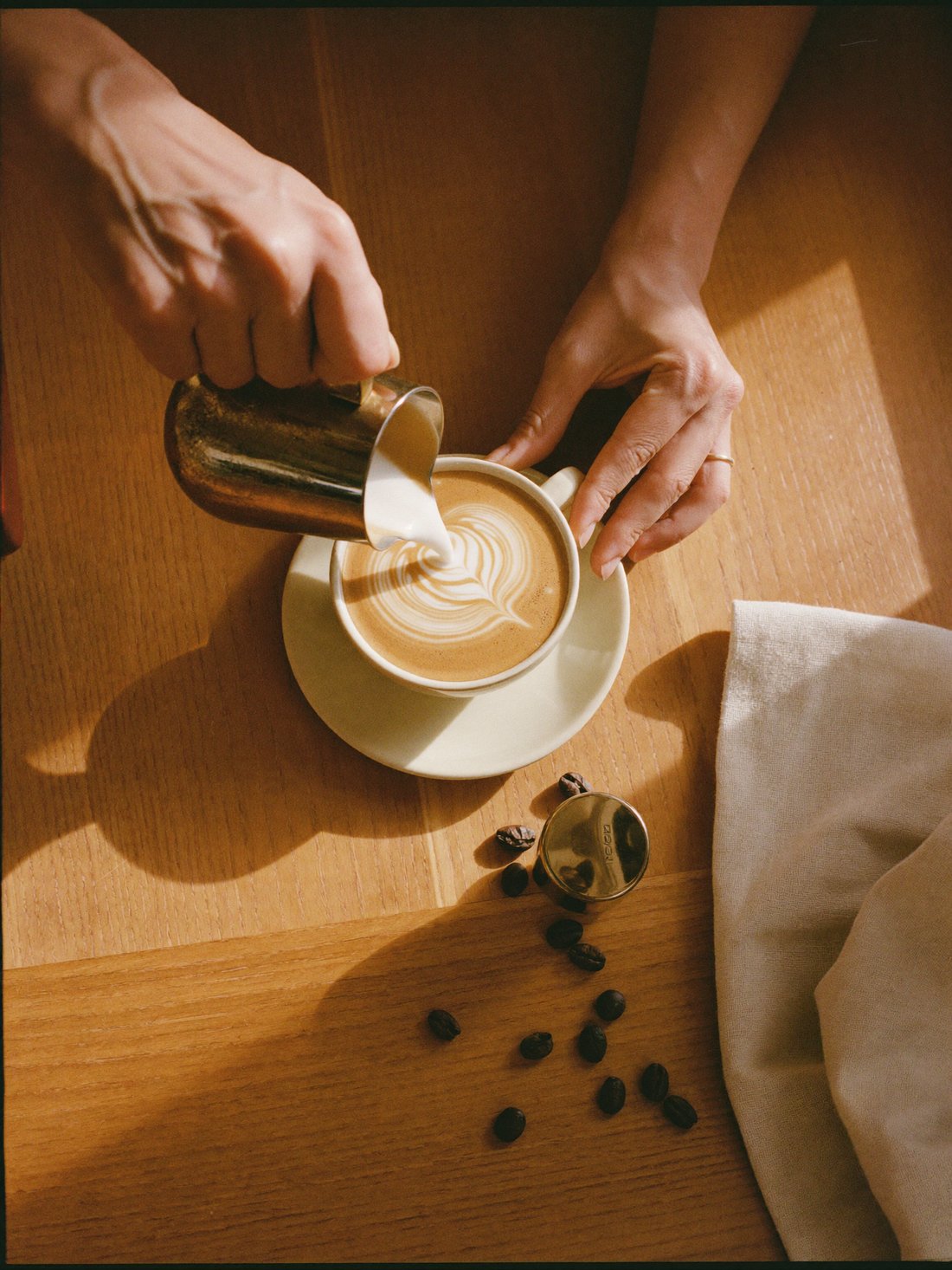 Mãos finalizando o desenho de um latte art em xícara de cerâmica