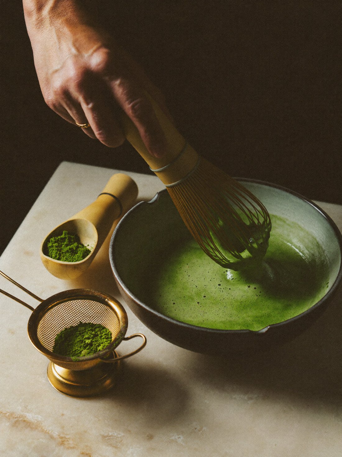 Matcha cerimonial sendo batido com chasen de bambu em tigela de cerâmica